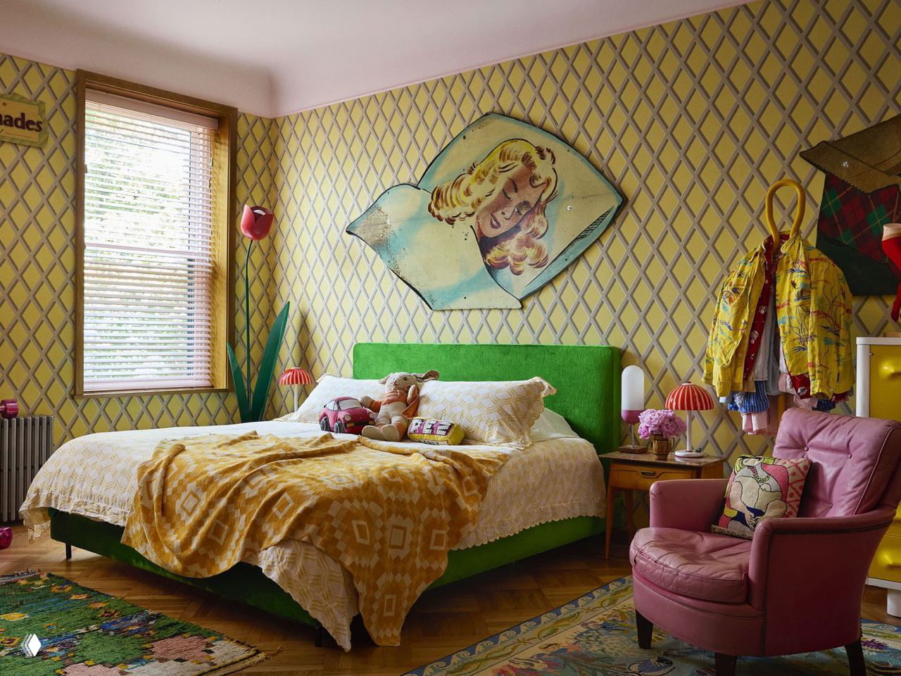 Спальня с зеленым изголовьем и желтыми узорчатыми обоями, мягкими текстурами и игрушками на кровати — уютный красочный интерьер.