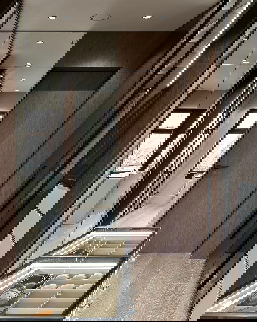 Гардеробная с стеклянными витринами и деревянной отделкой: подсвеченные секции для аксессуаров и аккуратно организованные ячейки хранения.