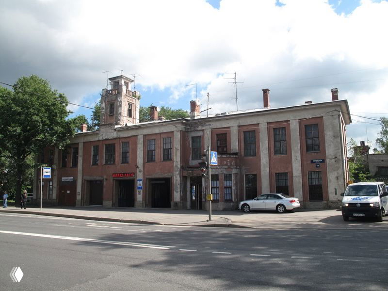 Невысокое промышленное здание на улице Петербурга с простым кирпичным фасадом, вывеской и редкими припаркованными машинами.