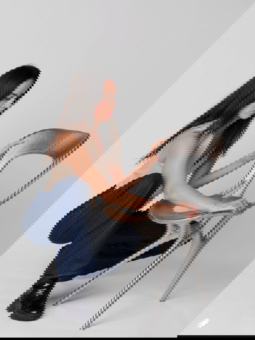 Женщина садится рядом с металлическим креслом из 3D-печати, примеряя посадку и оценивая форму сиденья и спинки в студийной съёмке.