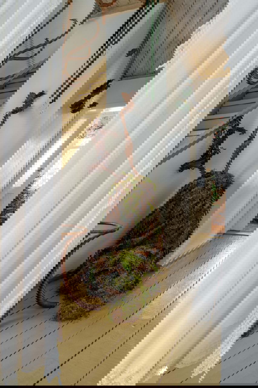 Интерьер коридора с большой инсталляцией из мха у лестницы и зелёными шариками на подвесах — сочетание природных материалов и винтажной мебели.