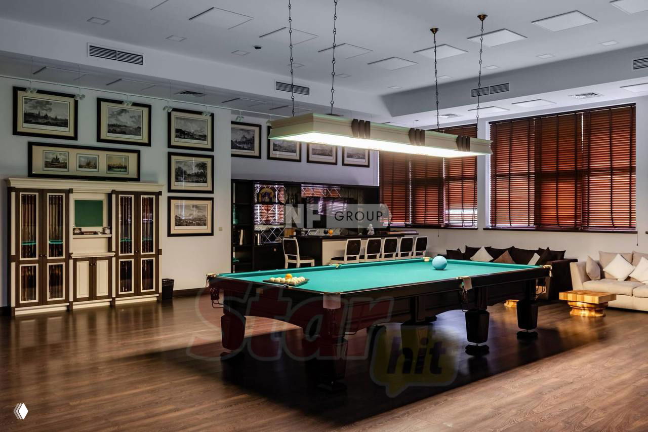 Интерьер бильярдной в одном из особняков: просторная комната с бильярдным столом, деревянным полом и зоной для отдыха гостей и друзей.