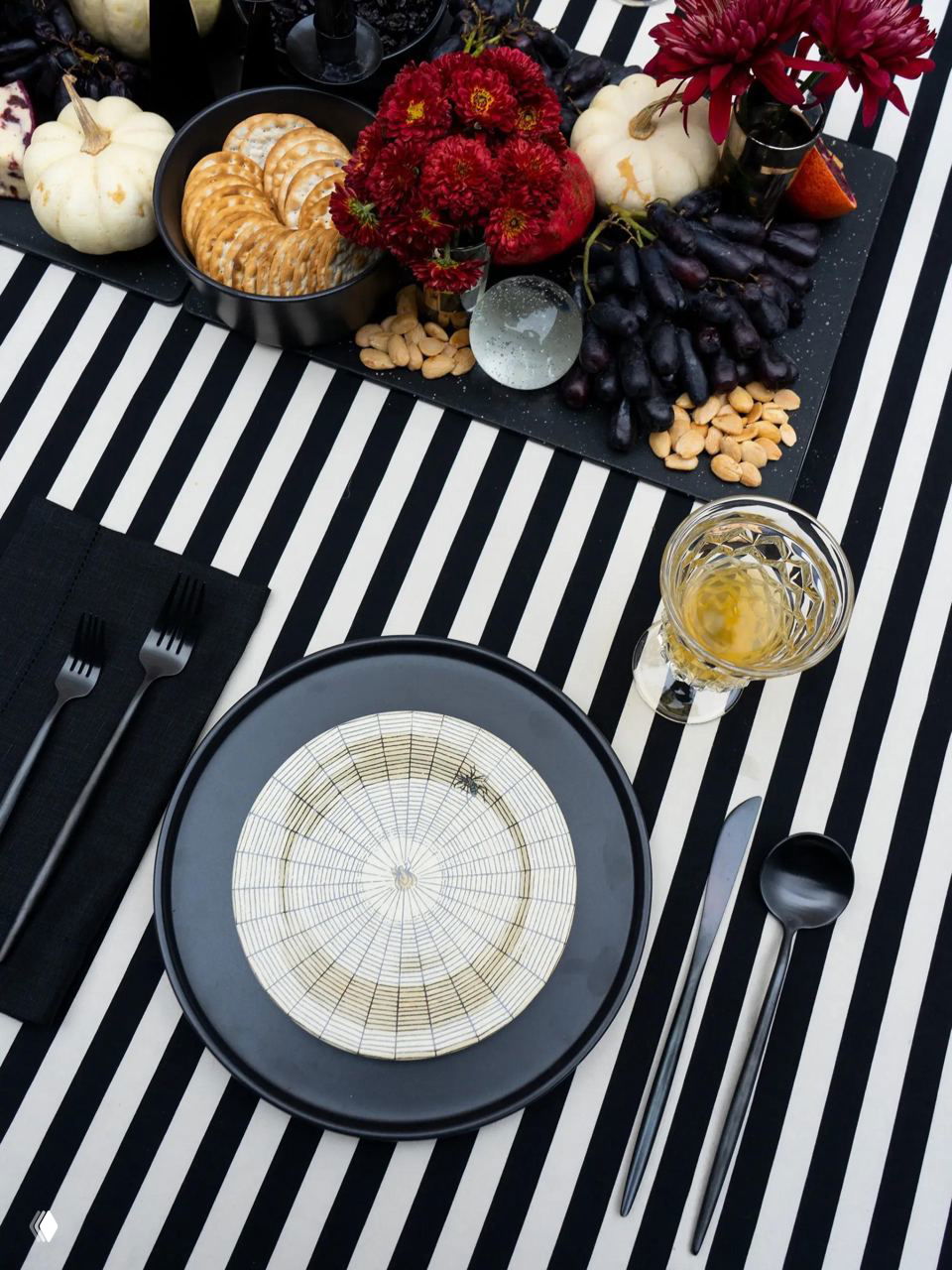 Стильная сервировка на полосатой скатерти: черная посуда, нарезки, белые мини-тыквы и темные виноград и орехи как элемент стола.