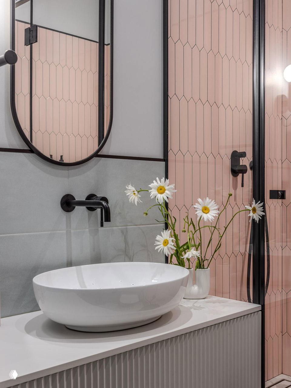 Ванная комната: белая раковина‑чаша на рифлёном тумбочке, розовая мозаичная плитка в душевой и букет ромашек на столешнице.