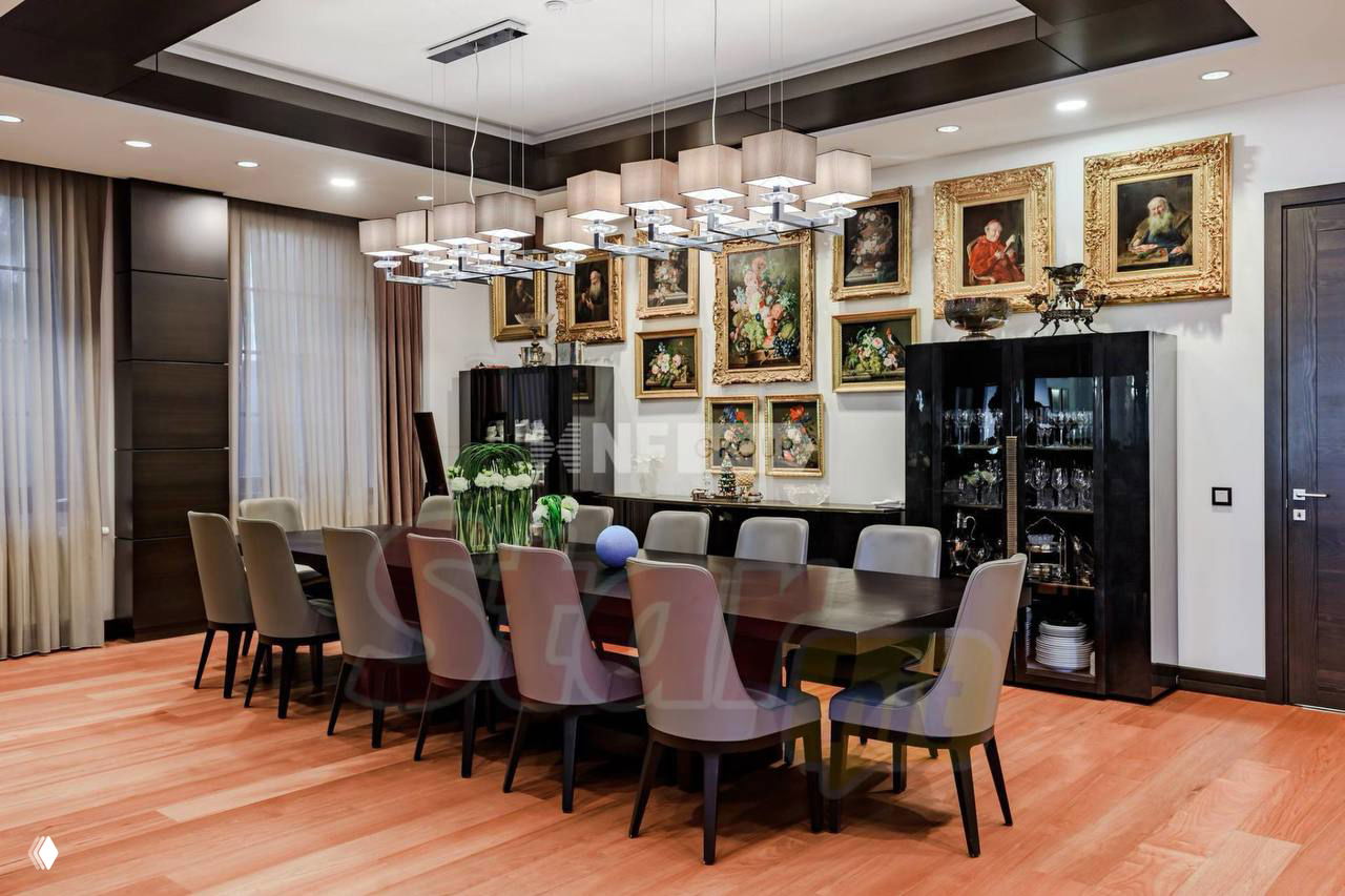 Столовая зона с большим обеденным столом, многочисленными картинами в золочёных рамах и современным освещением — интерьер для приёма гостей.