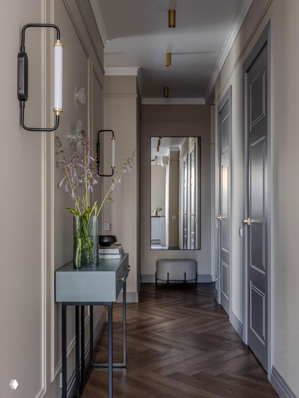 Прихожая с консолью, большим зеркалом в полный рост, настенными бра и длинным коридором с деревянным полом.