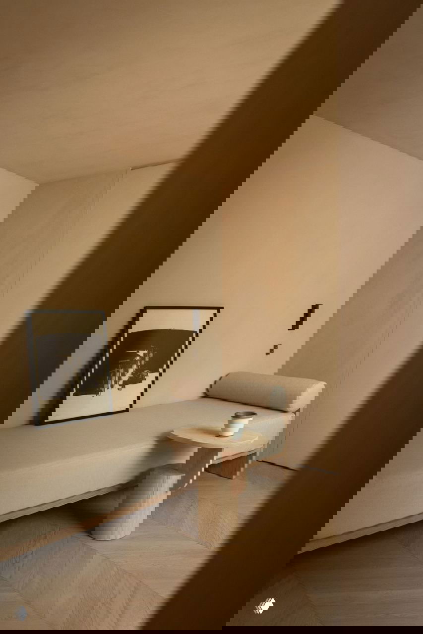 Минималистичная зона отдыха с длинным диваном, небольшим столиком и сдержанной монохромной эстетикой в бежевых тонах.