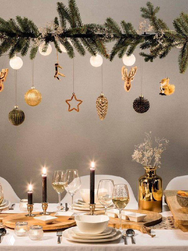 Камин, украшенный еловой гирляндой с золотыми и серебряными шарами, свечи и мягкая мебель — классический уют праздничной комнаты без традиционной ели.