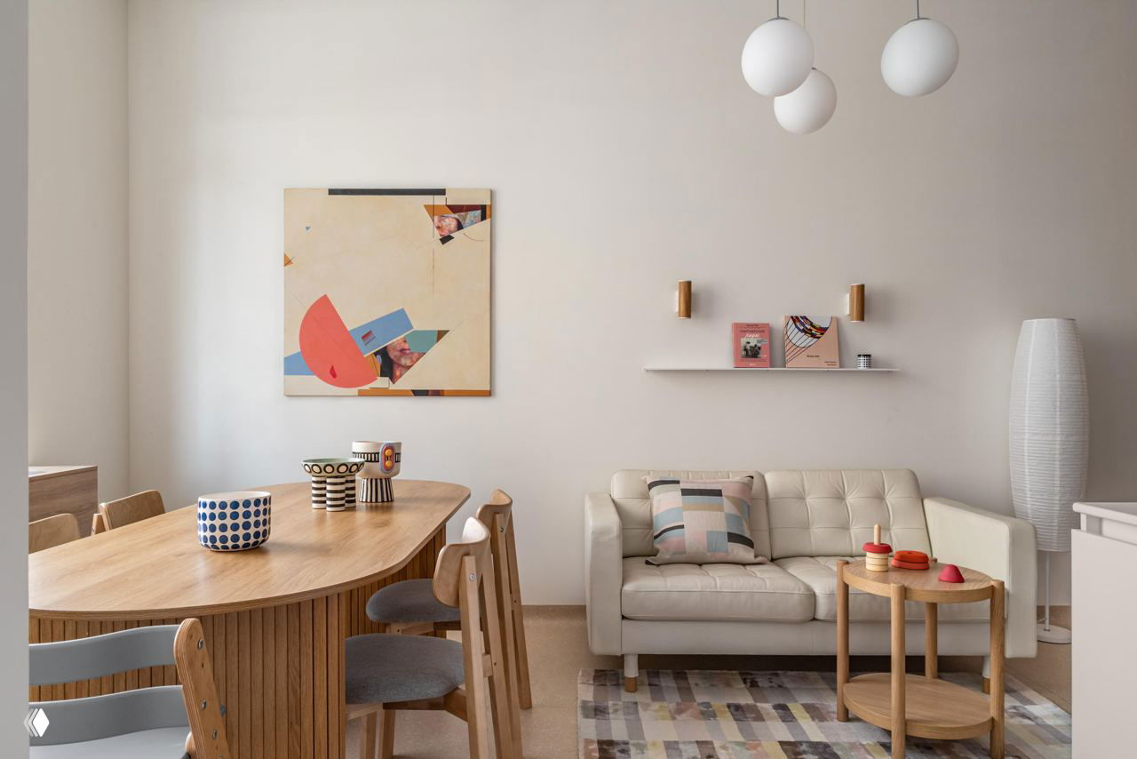 Интерьер клиники Киры Шаевой: светлая общая зона с деревянным столом, диваном, декоративной картиной и мягкой нейтральной палитрой, уютная атмосфера.