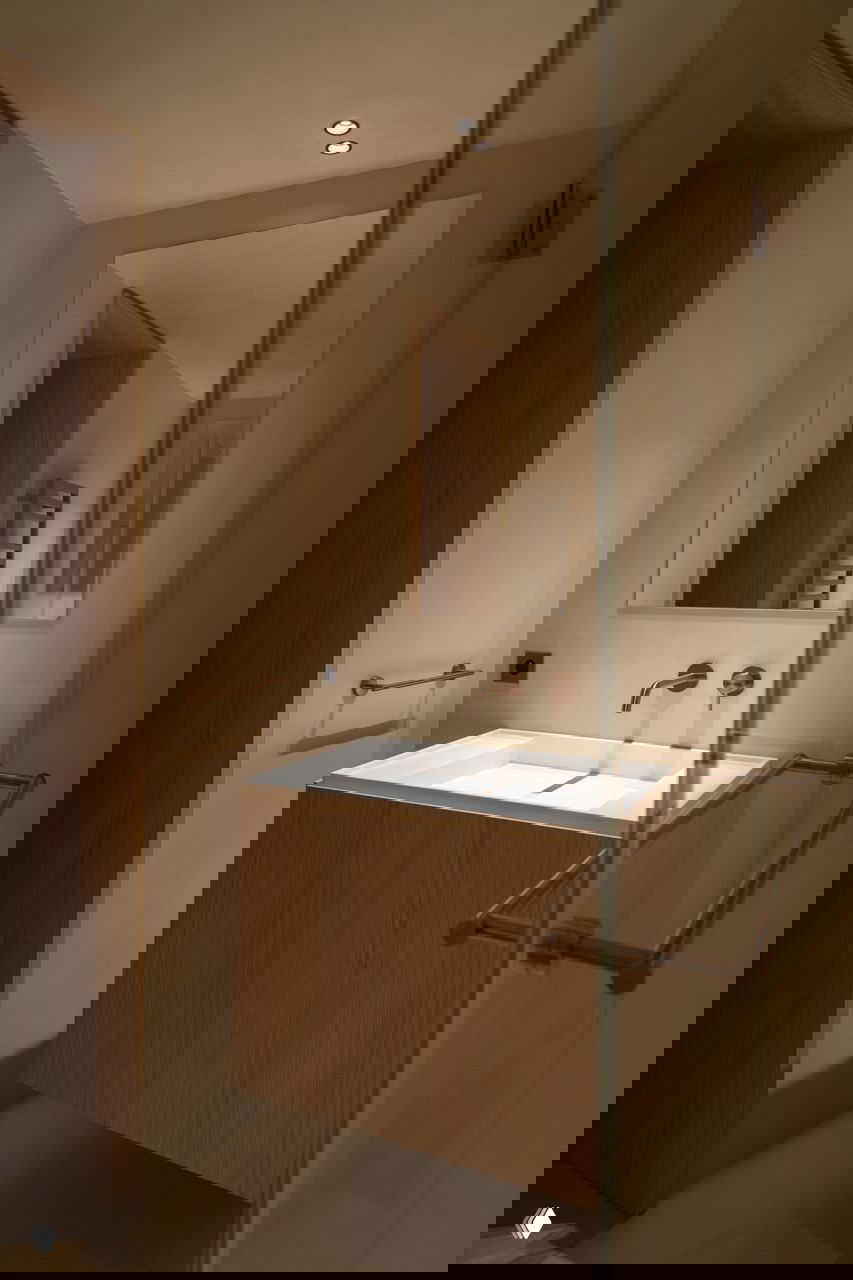 Ванная комната с деревянной тумбой под раковину, встроенной сантехникой и тёплым приглушённым освещением без ярких контрастов.