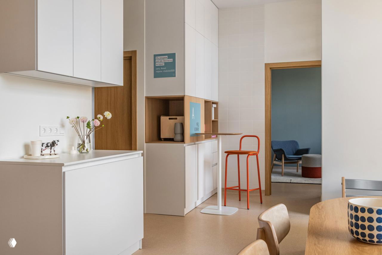 Зона ресепшена в клинике: белые шкафы и барный стол с ярким красным барным стулом — неожиданный прием в организации пространства для общения.