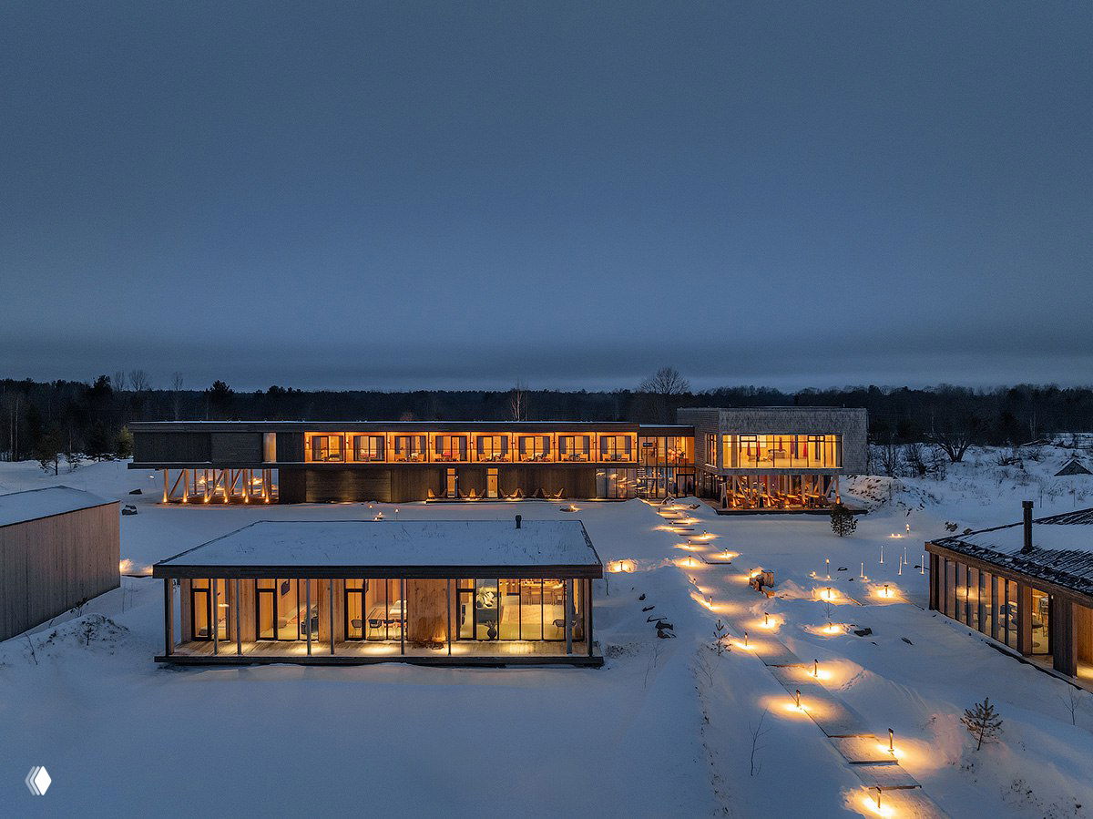 Панорамный вечерний вид на бутик‑отель «Заонежье» в Карелии: освещённые дорожки, гостевые корпуса с панорамными окнами и снег вокруг.