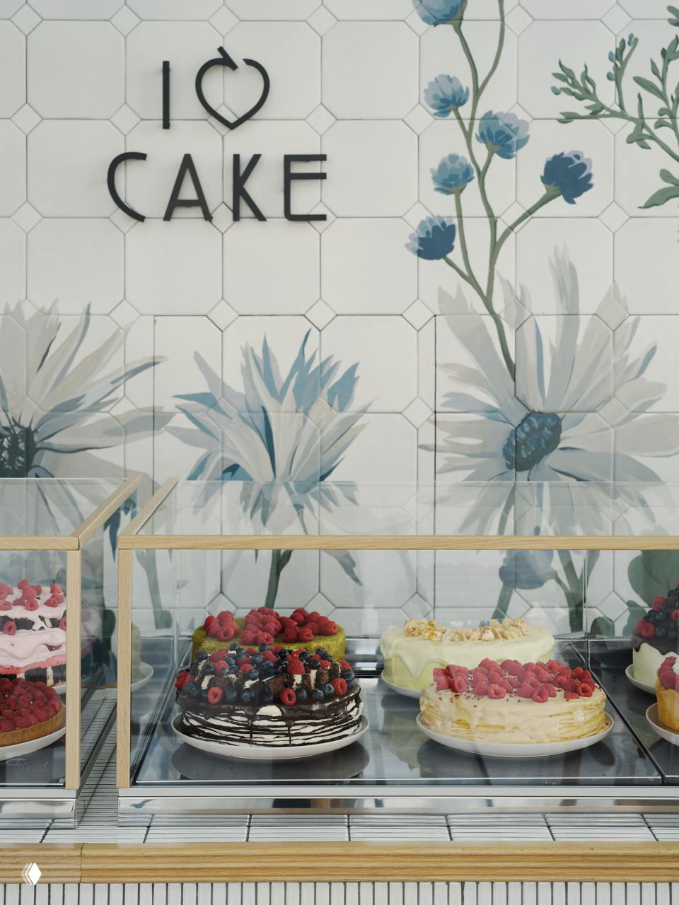 Близкий план витрины с тортами и ягодными десертами на фоне настенной росписи с крупными цветами в пастельных тонах, логотип I Love Cake