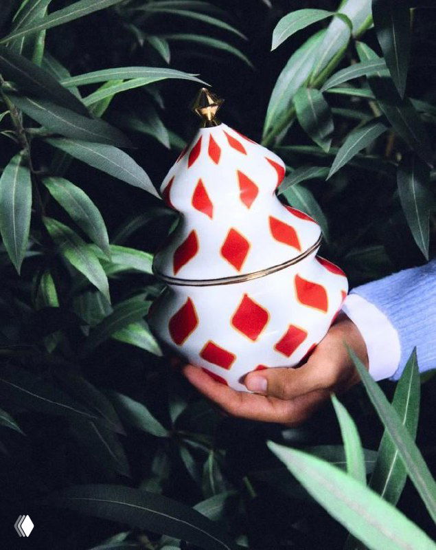 Крупный план елочной игрушки в окружении зелени и декоративных элементов — детали росписи и текстуры изделий Alessi в праздничной стилистике.