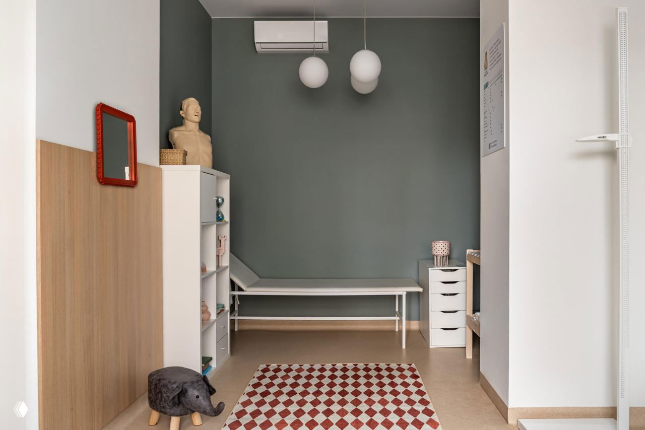 Малый кабинет осмотра с кушеткой и зелёной акцентной стеной; интерьер продуман для комфортного общения врача и пациента без визуального шума техники.