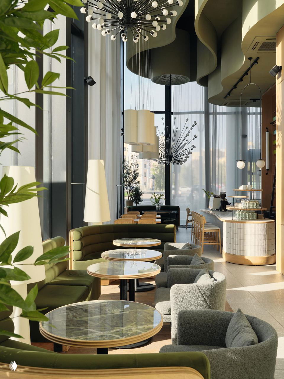 Зона посадки у больших окон: круглые столы с тёмно‑зелёными диванами, мягкие кресла и естественный дневной свет, создающий уютную атмосферу