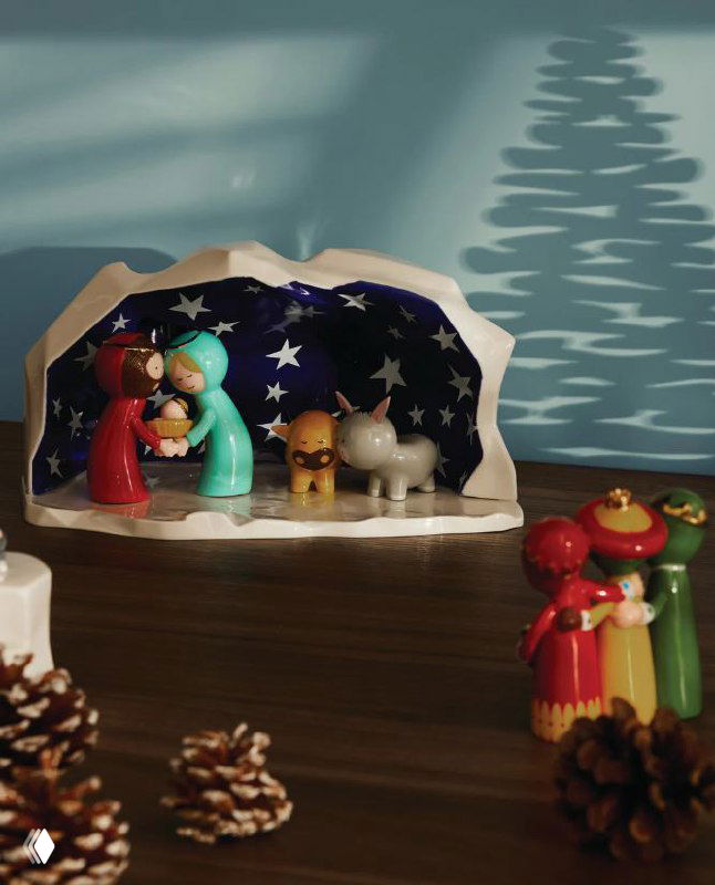 Миниатюрная рождественская сценка с фигурками в яслях и шишками на столе — элементы праздничной витрины и декора Alessi 2025/26.
