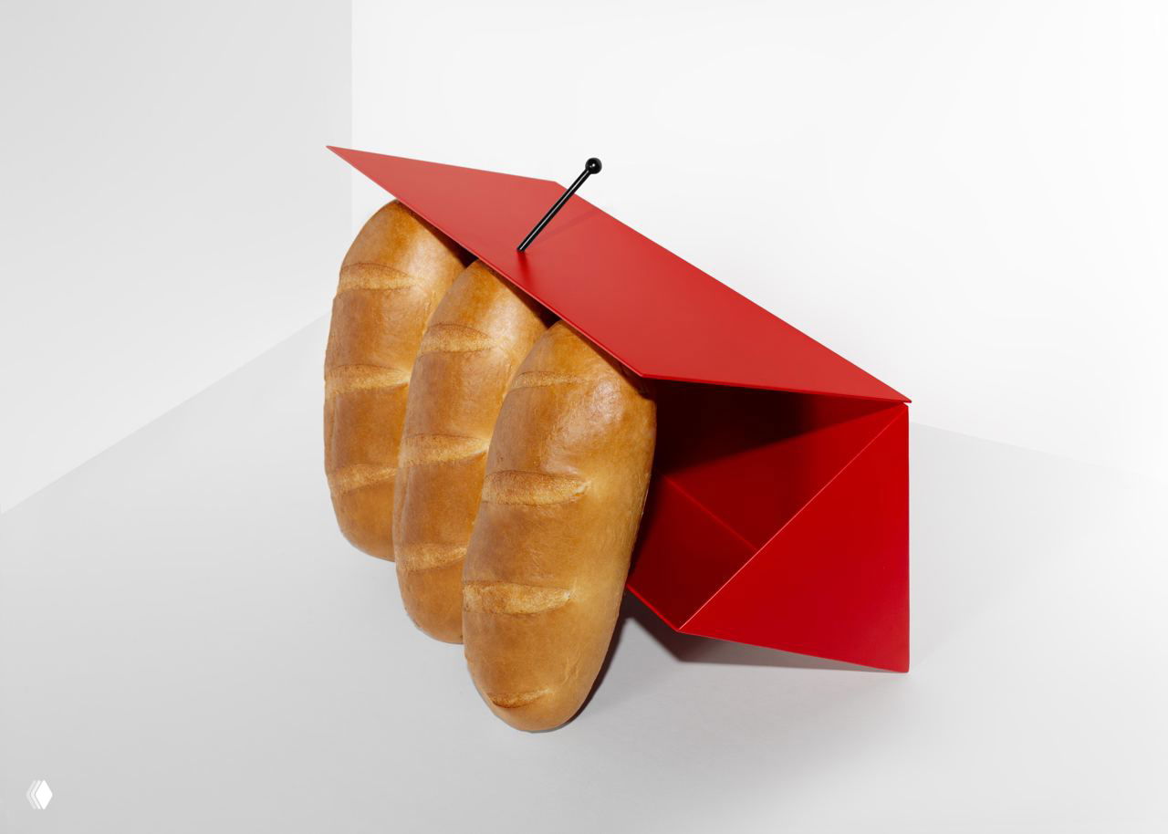 Вид под углом: хлебница «Зdobnitsa» закрывает три батона, красная стальная крышка и вертикальный чёрный стержень как центровая опора в композиции.