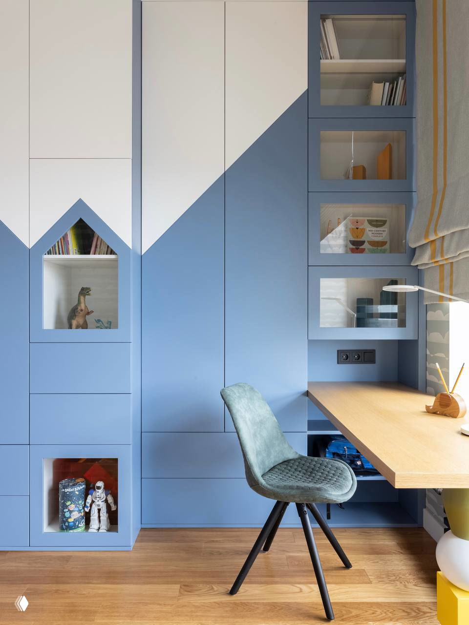 Голубой встроенный шкаф с геометрическими фасадами, открытыми нишами для книг и рабочим столом в уютной детской зоне.
