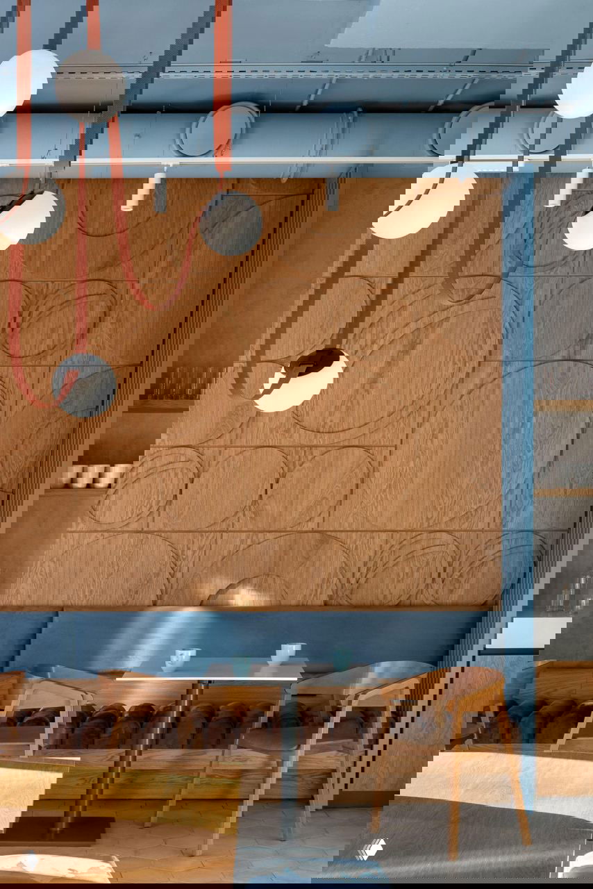 Деревянная рельефная панель в интерьере кафе, синяя банкетка, стол и деревянные стулья — спокойная палитра дерева и голубого.