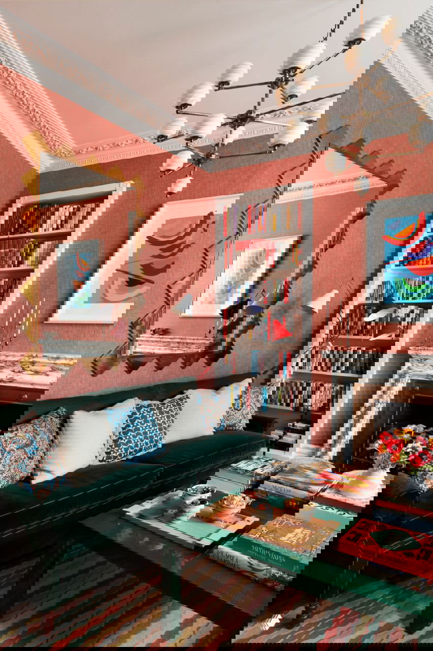 Гостиная с темно-зеленым бархатным диваном, мраморным камином, книжным стеллажом и яркими декоративными подушками в лондонской квартире.