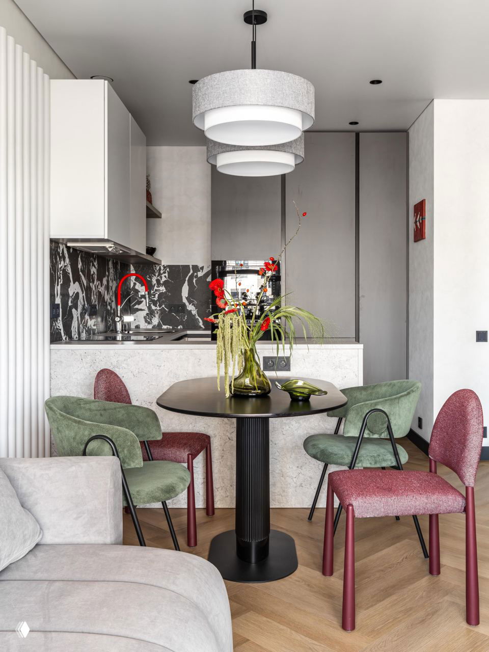 Общий вид кухни и столовой: круглый чёрный стол, сочетание зелёных и бордовых стульев, ваза с зелёными и красными акцентами на столе.