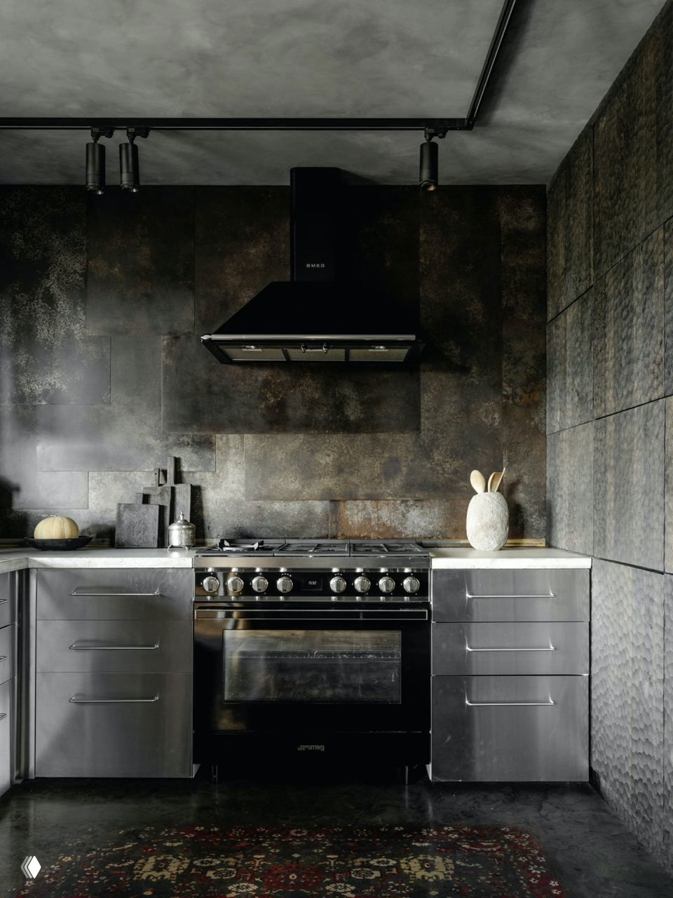 Кухня в строгой тёмной палитре: металлическая плита и монохромные фасады на фоне фактурной плитки и матового покрытия стен.
