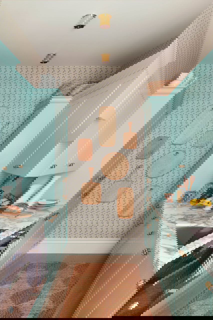 Узкая кухня в мятно‑бирюзовых фасадах, мраморная столешница, компактная планировка и декоративные разделочные доски на стене.