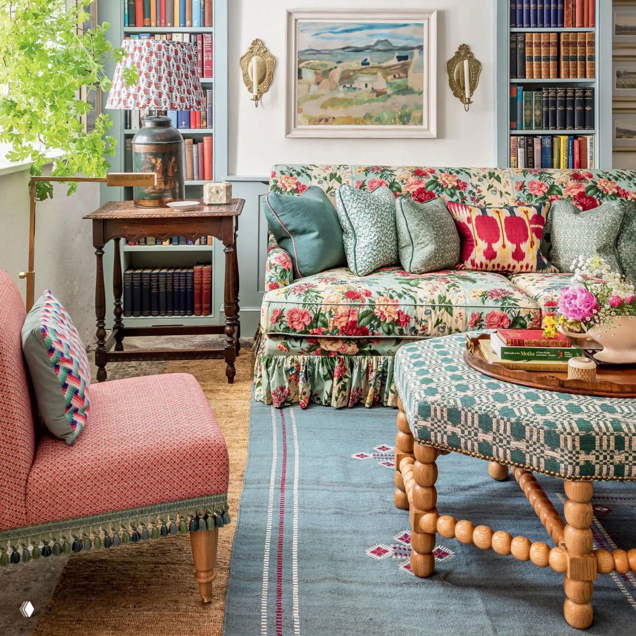 Уютная гостиная с цветочным диваном, книжными полками и круглым столиком на резных ножках; смешение узоров и материалов.