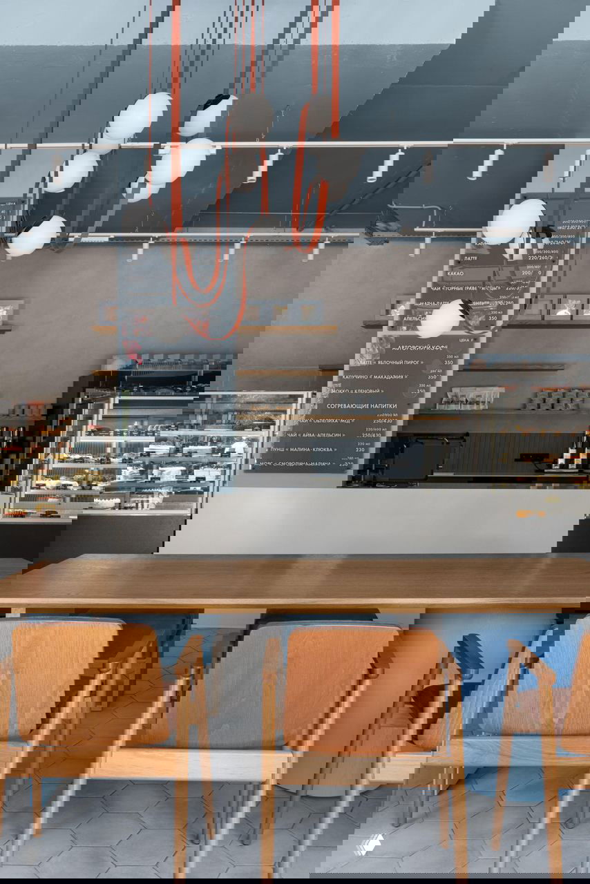 Барная зона и касса: длинный стол, деревянные стулья, подвесные круглые светильники и витрины с выпечкой за стойкой.