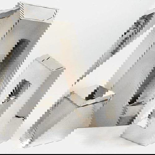 Крупный план полированной металлической формы сервиза с прямоугольным отверстием — минималистичная скульптурная посуда в духе Захи Хадид.