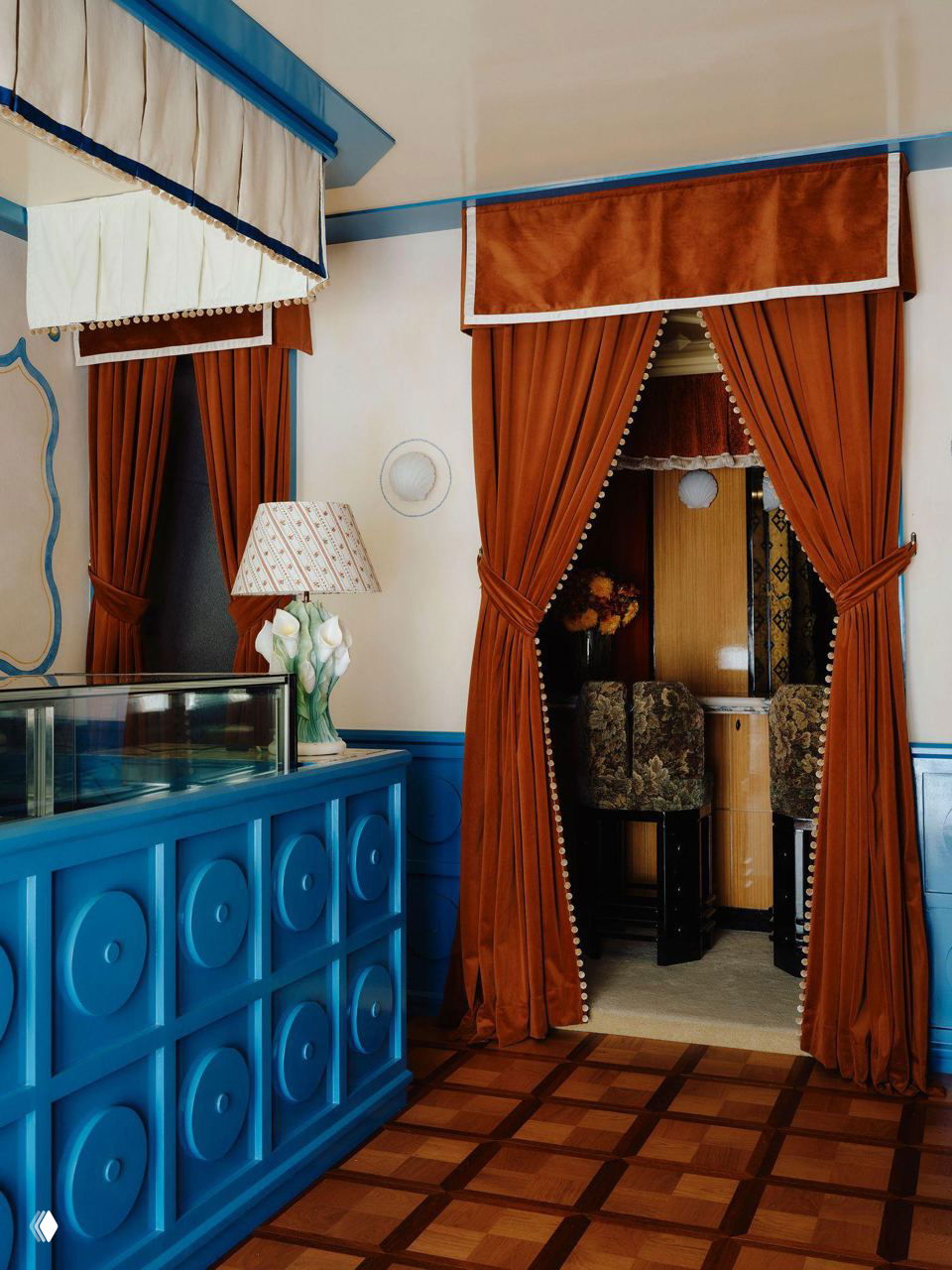 Интерьер у прилавка: насыщенно‑синий деревянный прилавок, декоративная лампа и тяжёлые бархатные шторы у входа в камерную зону.