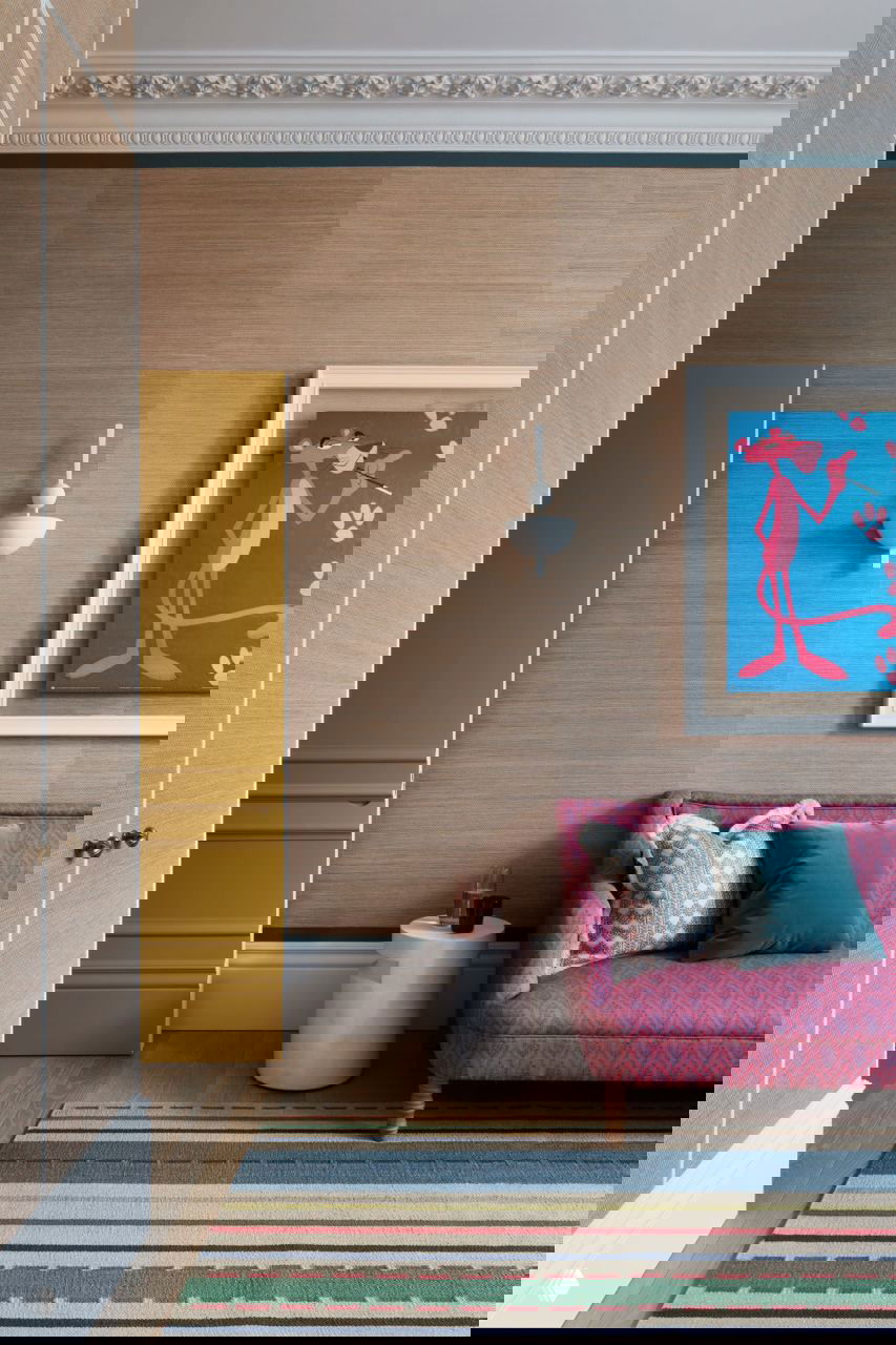 Комната с нейтральными обоями, розовым диваном, яркой картиной (персонаж Pantera) и декоративными подушками — игра цвета и фактур.