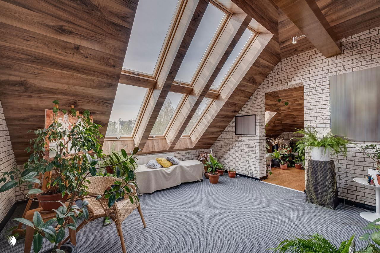 Мансардная зона отдыха с наклонными панорамными окнами, белой кирпичной кладкой, уютным диваном и несколькими горшечными растениями в интерьере.