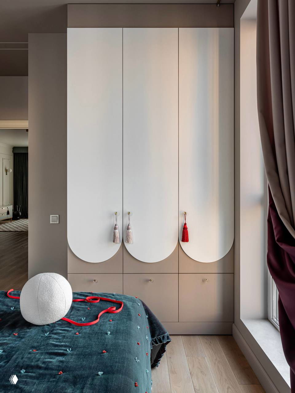 Белые шкафы с закруглёнными фасадами и декоративными кисточками‑петельками в детской или спальне, мягкая и игривая форма.