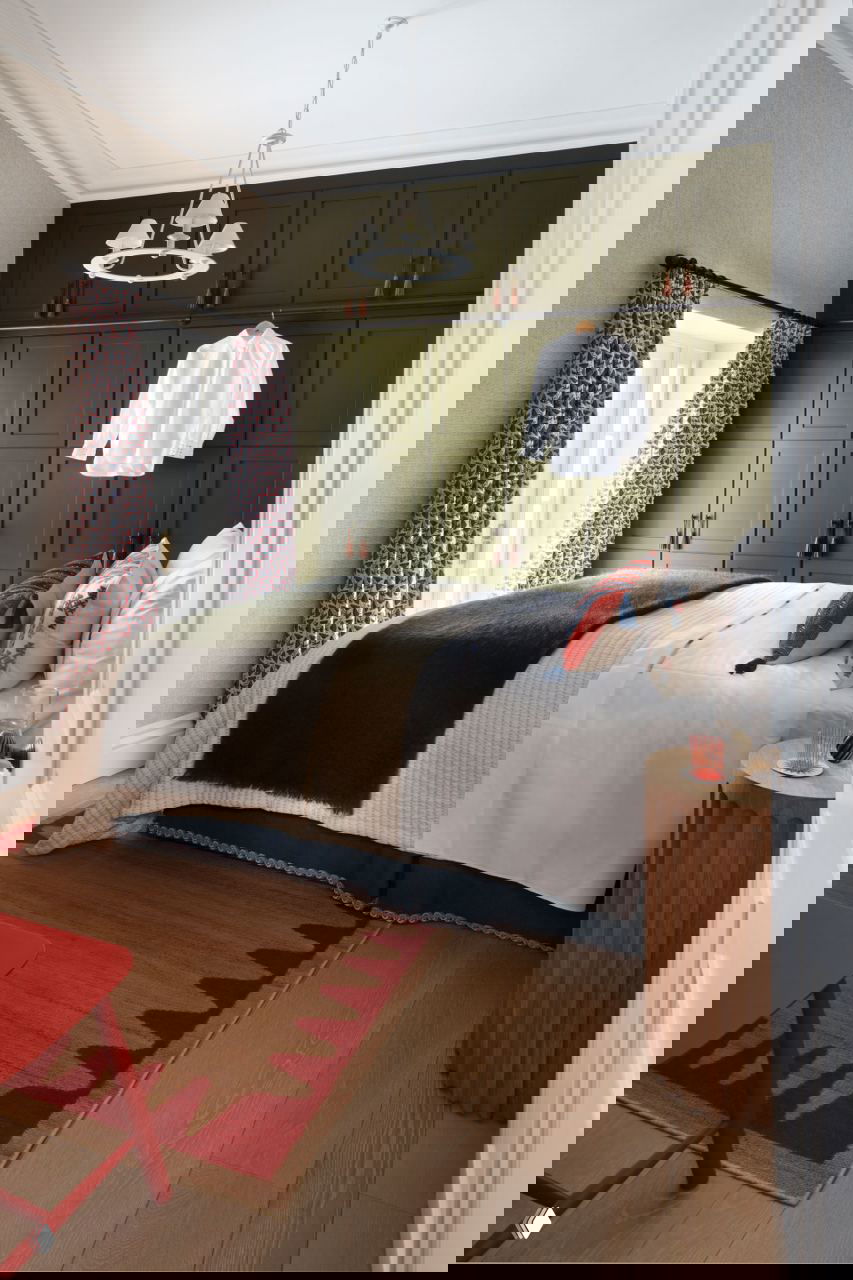 Спальня с блекло‑оливковыми встроенными шкафами до потолка, аккуратной кроватью с текстильными акцентами и натуральным деревянным полом.