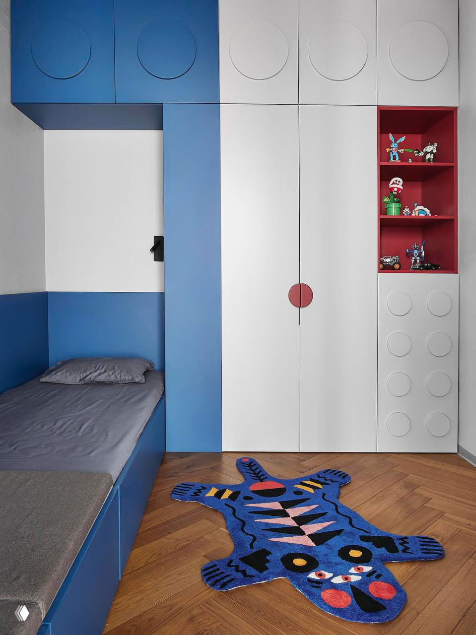 Игровой детский шкаф в стиле конструктора: синие и белые фасады, круглые декоративные вставки и открытые красные полки для игрушек.