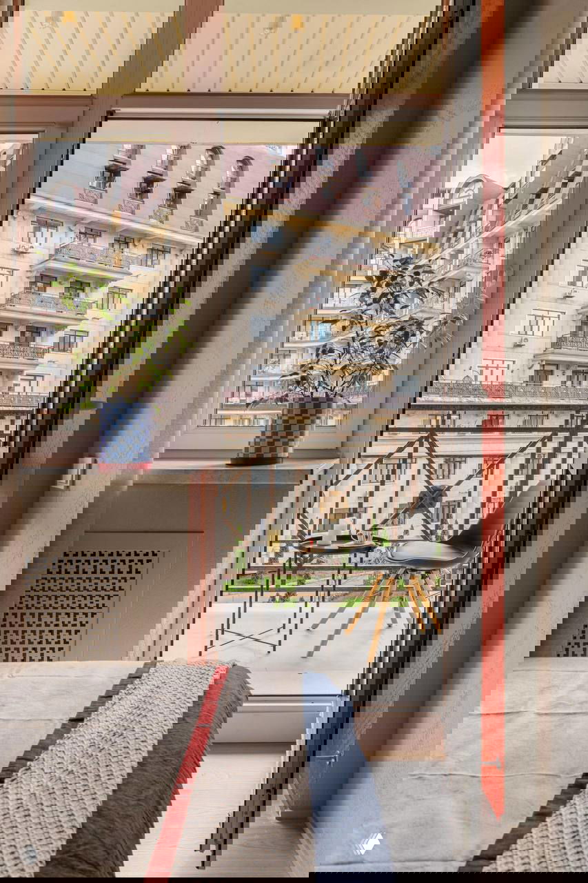 Открытый балкон с видом на городской фасад, небольшим столиком и стулом — продолжение спальни и дополнительная зона отдыха.