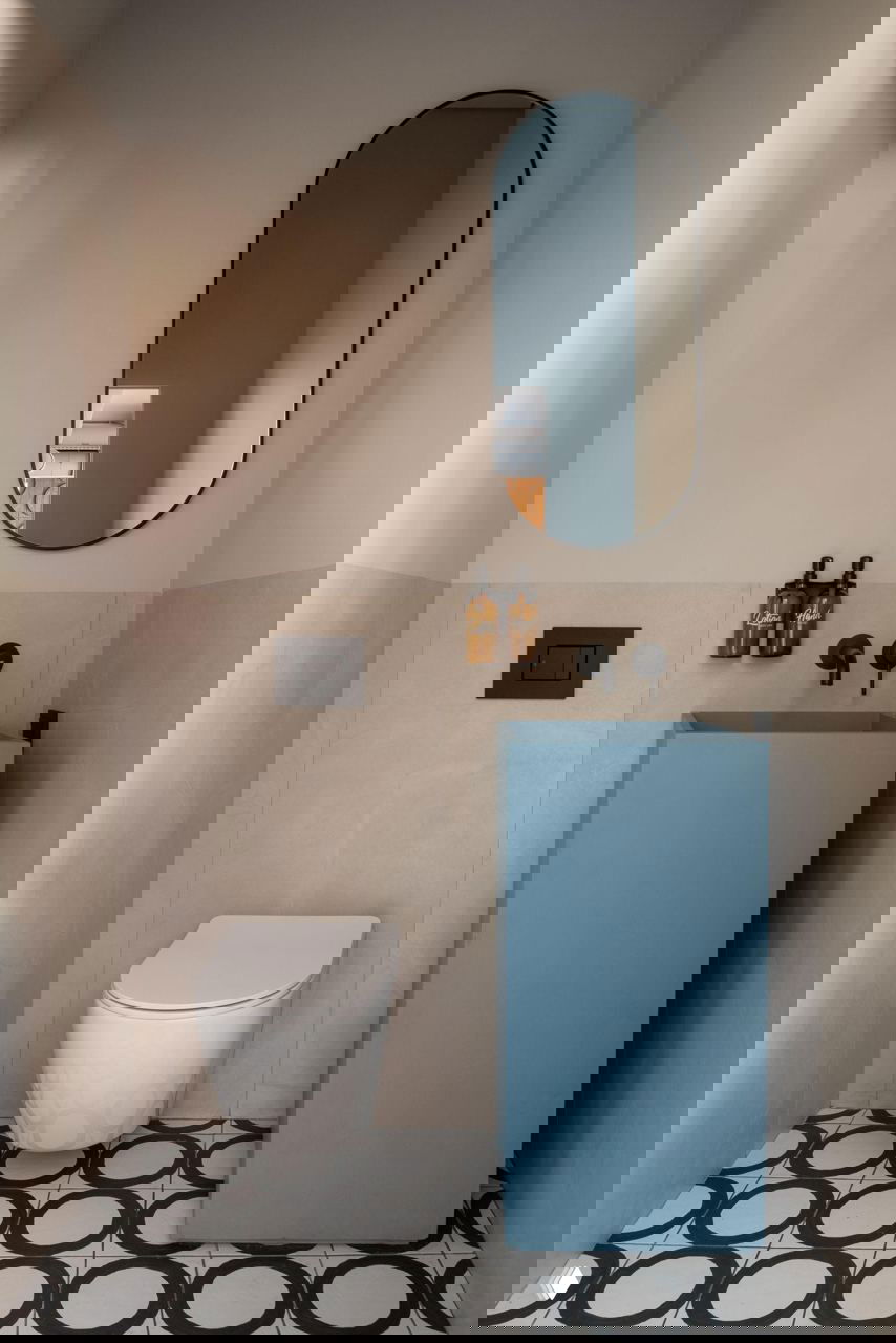 Небольшой санузел кафе: голубая тумба-раковина, зеркальная ниша и плитка с геометрическим узором на полу.