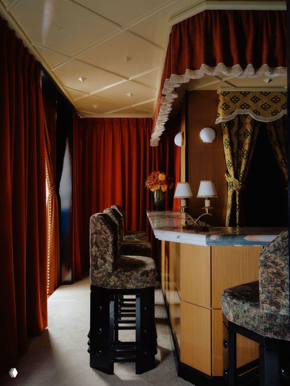 Крупный план барной стойки с мраморной столешницей, деревянной облицовкой и декоративной занавесью над зоной обслуживания гостей.