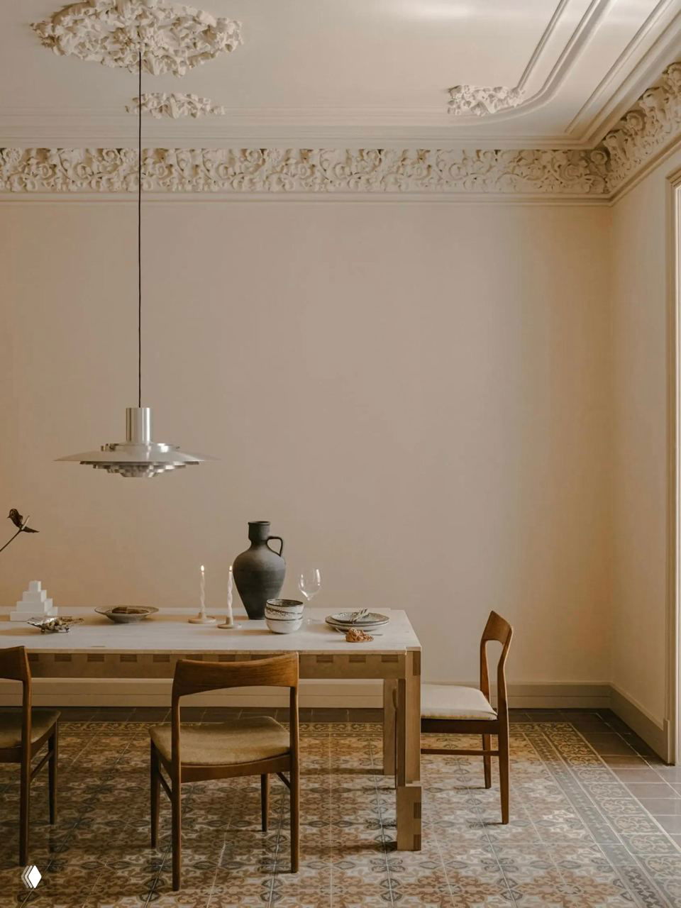 Столовая зона с тонкой цветочной карнизной лепниной и рельефной потолочной розеткой над светильником; деревянный стол и стулья в простом стиле.