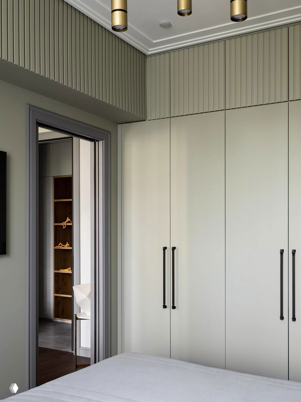 Минималистичный спальный шкаф с крупными тёмными ручками, светлыми фасадами и декоративным фризом в верхней части стены комнаты.