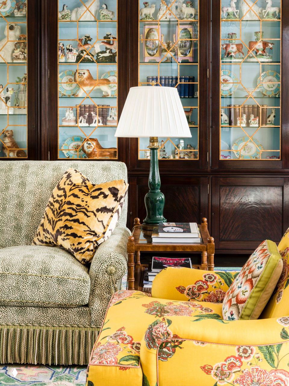 Интерьер в эклектичном стиле: диван светлых тонов с классической пышной бахромой, рядом журнальный стол и витрина с коллекционными предметами.