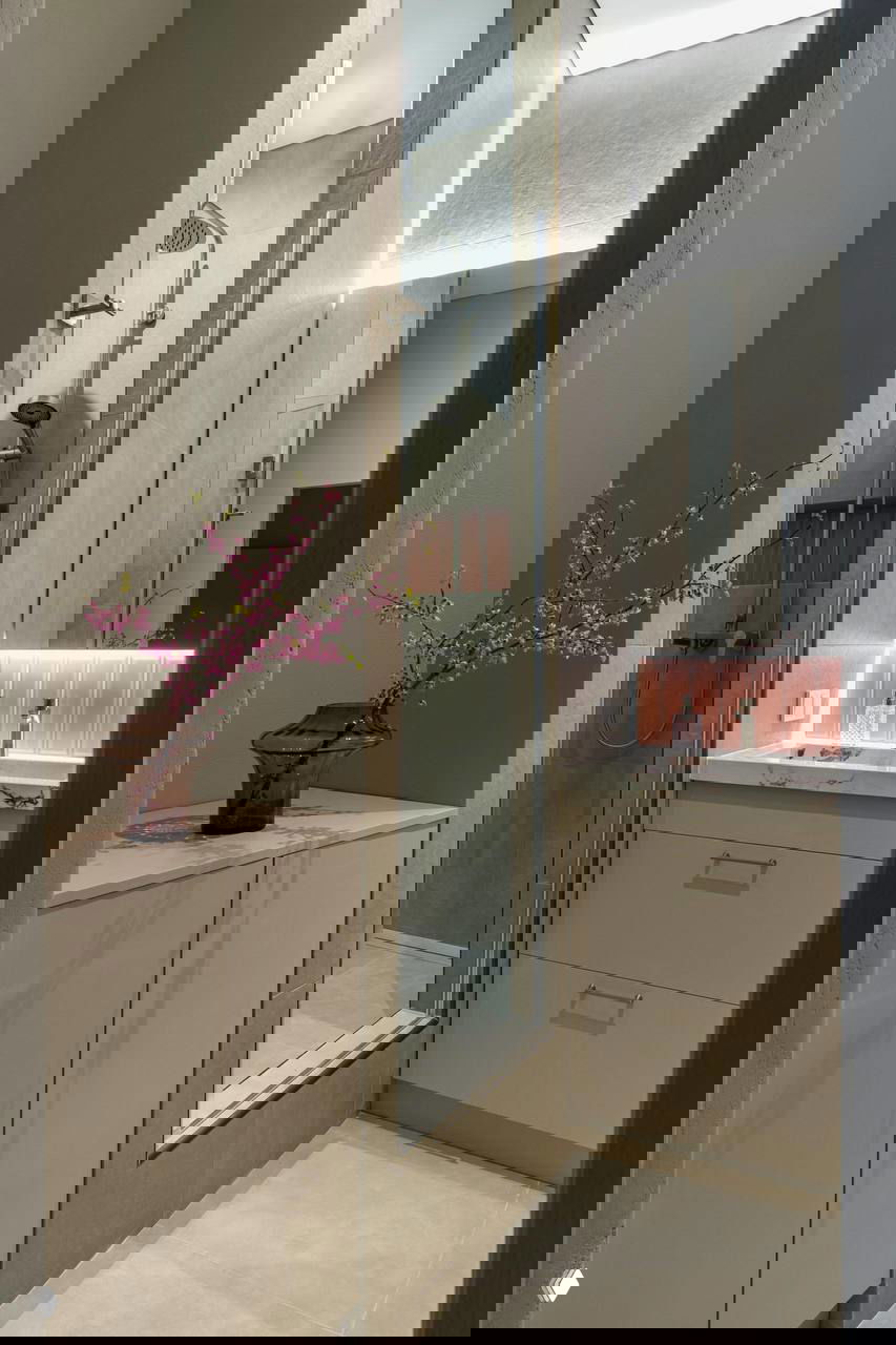 Компактная ванная комната с душевой кабиной в нише, зеркалом с подсветкой и нежными розовыми деталями у умывальника.