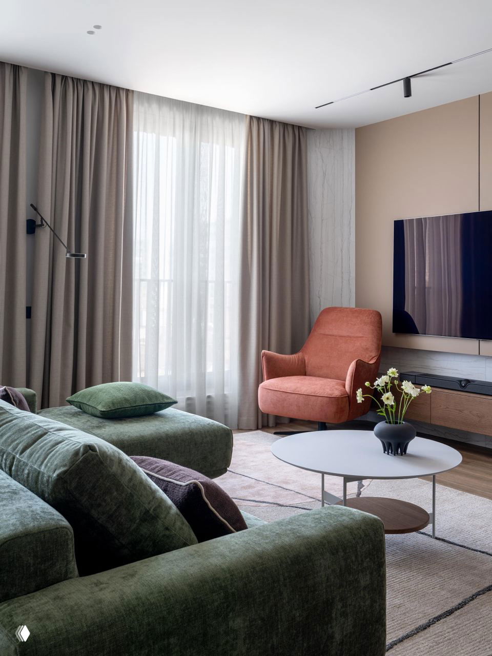 Широкий ракурс гостиной с зелёным модульным диваном, розовым креслом и круглым кофейным столиком у окна с тюлем — мягкая цветовая гамма.