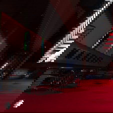 Тёмное или ночное фойе с красным ковровым покрытием и крупным пространственным залом, видна часть фасада и архитектурные детали внутри галерейного комплекса