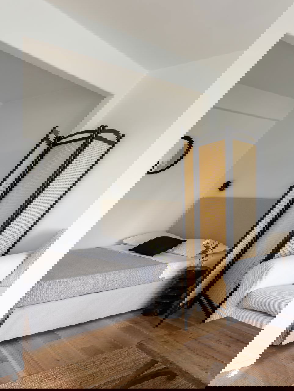 Угол спальной зоны: изголовье кровати, часть дивана на переднем плане и плетёная ширма чётко делят пространство небольшой квартиры-студии.