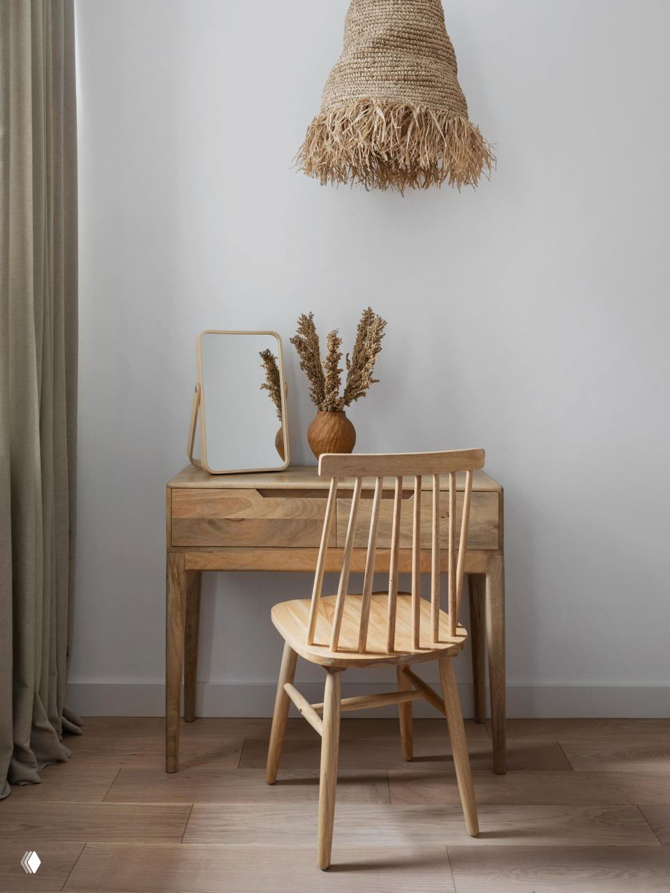 Небольшой рабочий уголок: деревянный столик, плетёный подвесной светильник и ваза с сухоцветами — акцент на простоте и материальности.