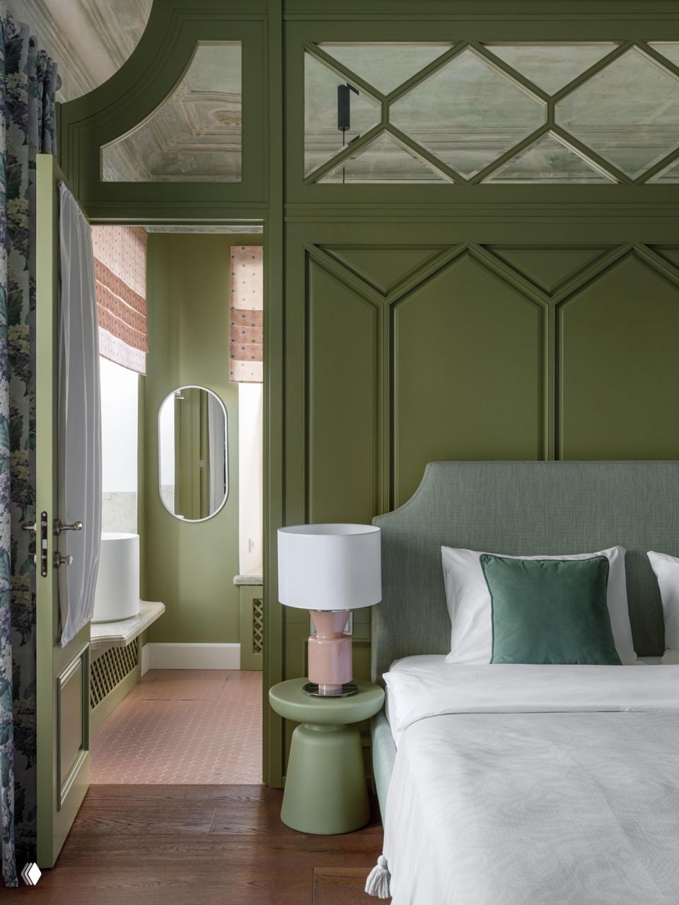 Спальная зона с панелированными зелёными стенами, мягким изголовьем, прикроватной лампой и видом на архитектурные элементы и оформление в духе XIX века.