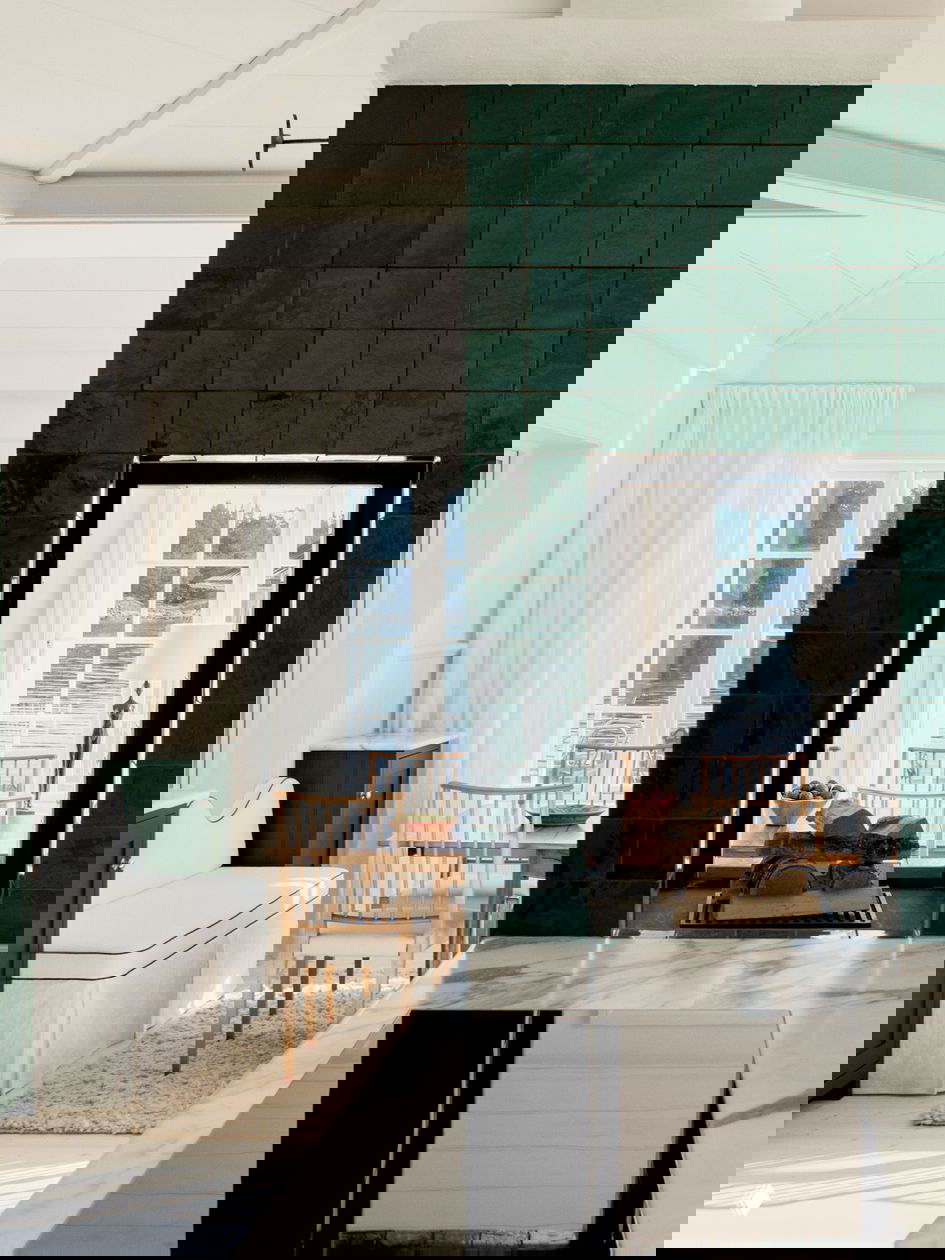 Кухонный вид через зелёную плиточную перегородку: мраморная столешница на переднем плане и столовая зона у окна с видом на море.